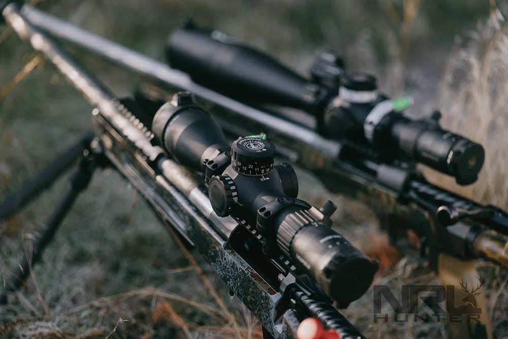 Precision hunting rifles and optics staged in field grass